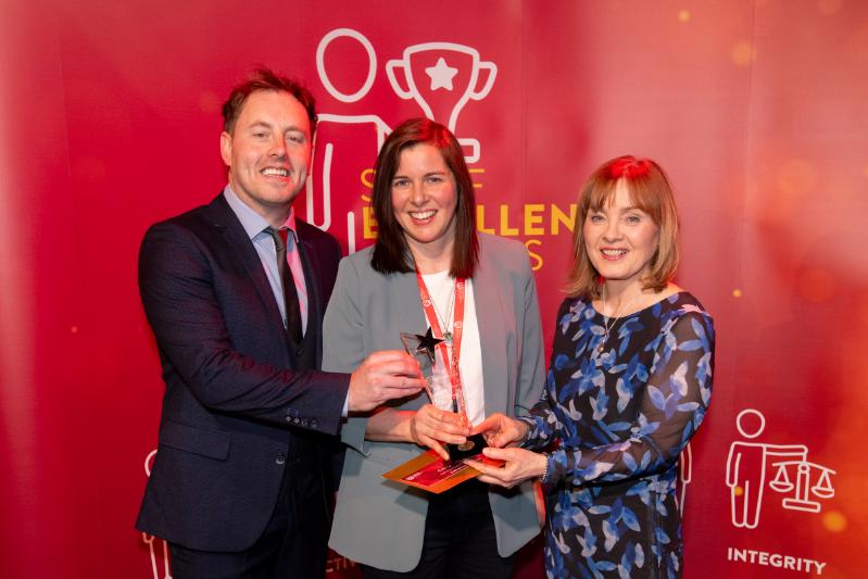 two women and one man, smartly dressed, in front of a red background